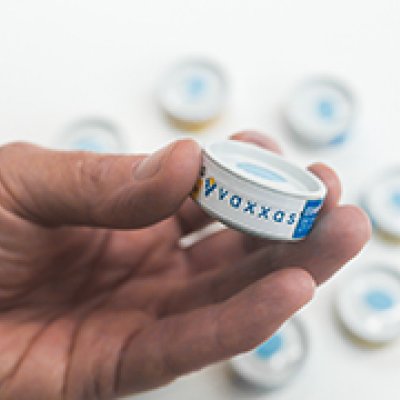 A hand holding a cannister containing the vaccine patch.